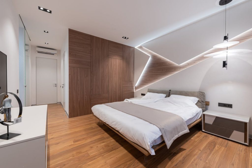pexels-photo-6186810 Light modern hotel room interior with soft white bed and wooden floor near cupboard